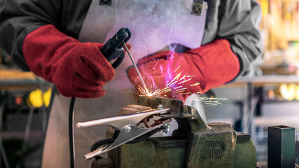 Craftsman working with arc welding machine in workshop. Piece of iron with spark