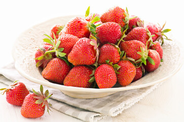 Reife rote Erdbeeren aus biologischem Anbau als close-up in einer rustikalen Design Schale auf einem weißem Board