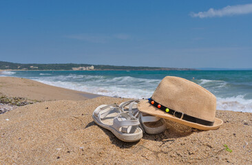White summer sandals and a straw hat on a sandy beach in the background the sea and the beach
