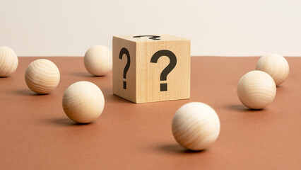 wooden cube with a question mark surrounded by wooden balls on a brown table background