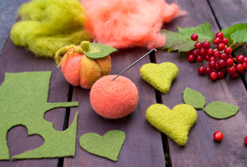 Pumpkin made using the dry felting technique, details and materials for making a felted pumpkin and two hearts made of wool on wooden boards surrounded by viburnum berries