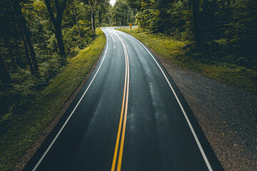 Fototapeta premium New road. Fresh asphalt on highway or freeway. Empty without traffic of car or truck roadway. Yellow double solid line. Country road passes through green forest. Atmospheric in dark colors photo.