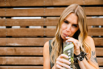 Woman sipping a cocktail in front of wood backdrop looking into camera, room for copy