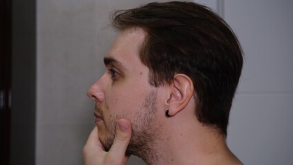 Fototapeta premium Young man examining his face while watching into the mirror