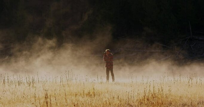Man walking and taking photos in grass field in Yellowstone National Park