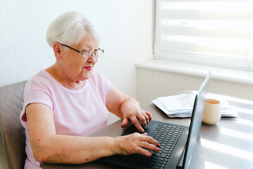Smiling Aged Woman Relaxing In Kitchen With Laptop And Tea, Browsing Social Media Or Reading News Online, Free Space
