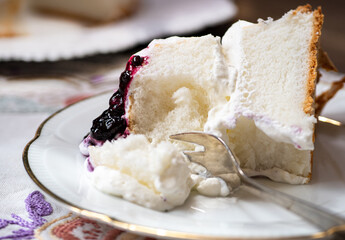 Slice section of angel food cake on white board sliced and filled with whipping cream, topped with summer berries