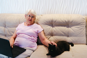 Obraz premium happy elderly woman using laptop computer at home. Senior mature older woman watching business training, online webinar on laptop computer remote working or social distance learning from home. 60s