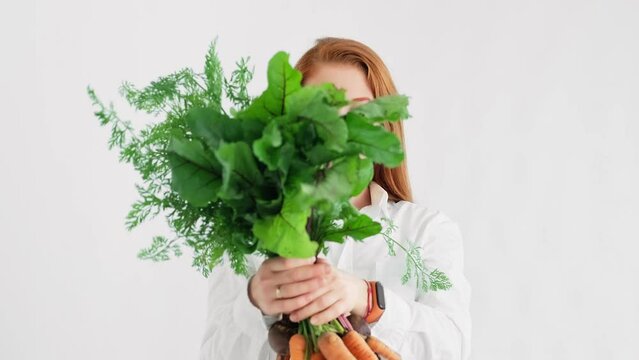 Young redhead woman with vegetables at white background. Carrot and beet in hand of cute female. Portrait of vegan woman. Healthy lifestyle. Green nutrition. 4K, UHD