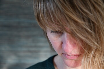 Close up of the head of a caucasian woman with blond hair looking down. Sun shining