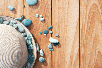 Elegant vintage straw hat with small blue sea pebbles on the wooden table. Summer and beach accessories. Copy space for text