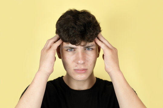 Sad Cute Teenager Boy On Yellow Background Holding His Head, He Has A Headache From Overwork And His Whole Face Is Covered With Pimples, Medical Concept, Teenage Skin Care