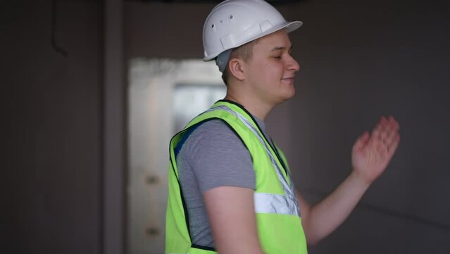 Cheerful positive builder dancing in building under construction having fun on break. Portrait of joyful Caucasian man in hard hat and green vest in new flat indoors. Excitement and building concept