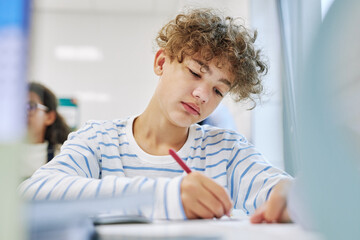 Low angle portrait of curly haired schoolboy taking test in school classroom