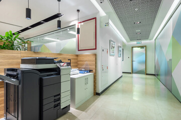 Bright office hall with tile flooring, glass door and office copy equipment.