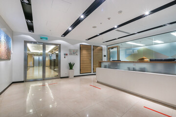 A spacious, bright office hall with a reception desk, glass doors and a picture on the wall. Red...