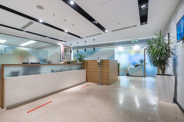 A brightly lit spacious office lobby with glass walls and a reception desk. Red line markings for...