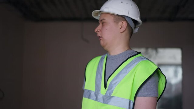 Overworking exhausted young builder yawning shaking hand leaving new apartment under construction. Portrait of tired Caucasian man walking away. Building and exhaustion