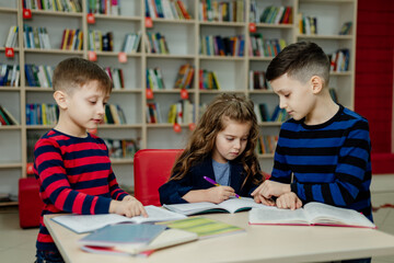 Fototapeta na wymiar school children in the library reading books, doing homework, prepare a school project for lessons