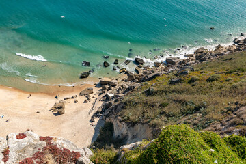 Obraz premium Rocks and sandy beach on the cliffs of the tourist resort of Nazare on the Atlantic coast of Portugal