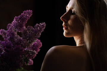 profile of a beautiful blonde woman with a bare shoulder and a bouquet of lilacs