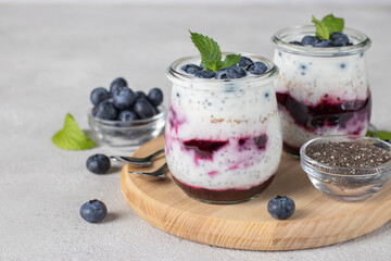 Chia pudding with blueberry and jam in two glass jars on wooden board on gray background, Close-up