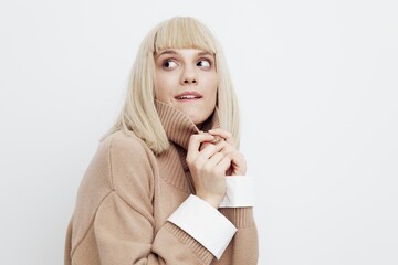 a beautiful happy woman stands on a light background in a sweater and shirt, looking around in surprise with her hands leaning against her face