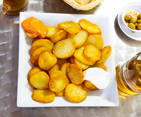 Delicious baked in oven yellow spicy potatoes bravas served at plate in cafe