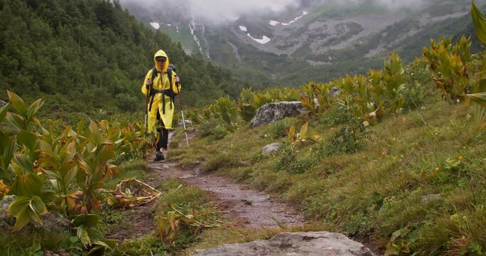 Woman hiker in yellow raincoat hiking in valey in mountain