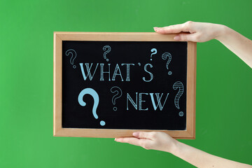 Female hands holding chalkboard with text WHAT'S NEW? on green background