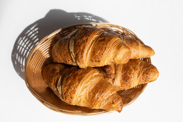 Fresh croissants in a wicker basket in the bright rays of the sun. Fresh pastries for breakfast. Home baking, bakery.