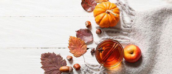 Composition with cup of tea, autumn leaves, pumpkin and scarf on white wooden background, top view