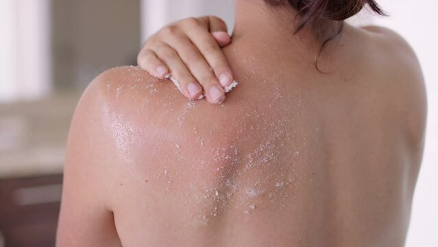 Woman exfoliates upper back and shoulder with white salt exfoliating scrub