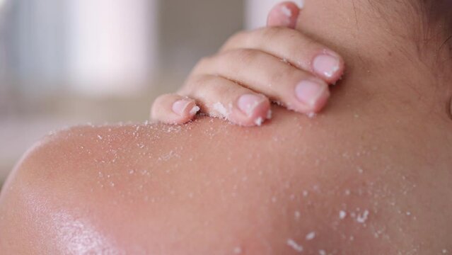 Woman exfoliates and rubs shoulder and neck with white exfoliating scrub 