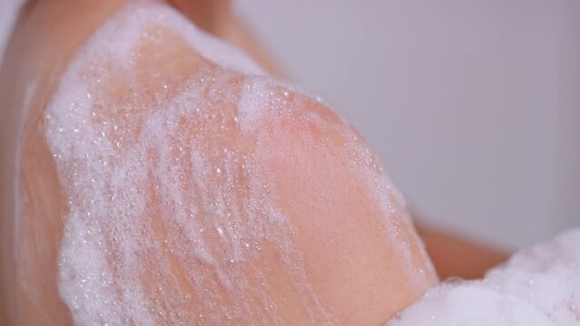 Extreme close up on body wash bubbles on woman's shoulder in shower