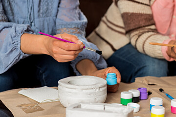 a woman's hands decorating a flower pot with paint.
