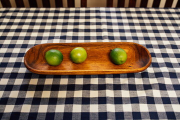 Limes in wooden dish on blue and white check tablecloth