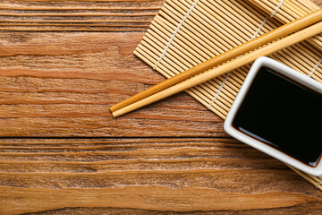 Bowl of soy sauce, chopsticks and bamboo mat on wooden background