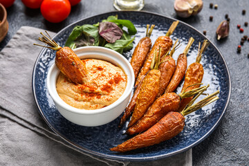 Plate with tasty baked carrots and bowl of sauce on table, closeup