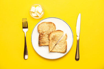 Plate with toasts, butter and cutlery on yellow background