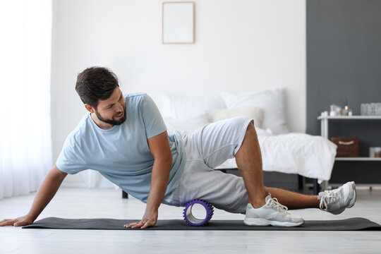 Young man training with foam roller in bedroom