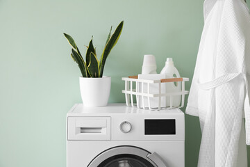 Basket with detergent and houseplant on washing machine near green wall