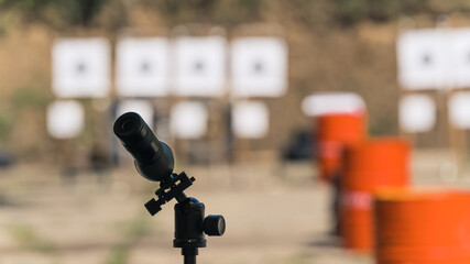Field glass at outdoor shooting range. Blurred background of targets and red barrels. Firearms training equipment. Outdoor horizontal shot. High quality photo