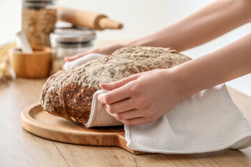 Young woman putting napkin with fresh bread onto board on light background, closeup