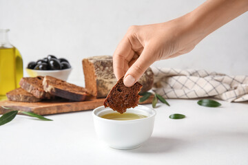 Woman eating slice of bread with olive oil on light background, closeup
