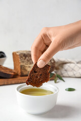 Woman eating slice of bread with olive oil on light background, closeup