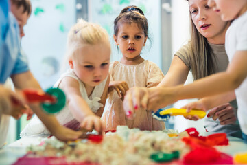 Fototapeta premium interested kids making kinetic sand figures with their teacher at the nursery. High quality photo
