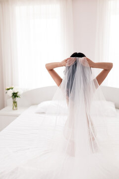 Bride getting ready for the wedding ceremony. A young woman fixes veil in her hair. The concept of boudoir photography. Selective focus, vertical orientation