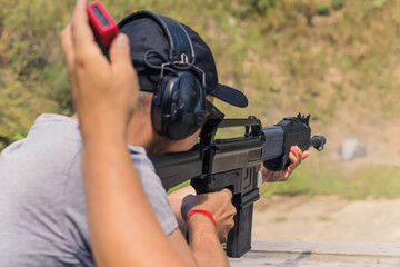 Rear view of man wearing safety headphones practicing firing shotgun on shooting range. Horizontal...