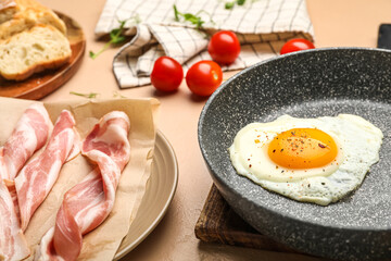 Plate of raw bacon and frying pan of tasty fried egg on table, closeup
